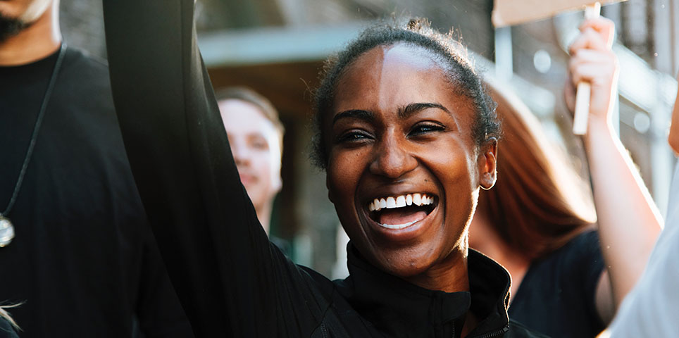 Young smiling black woman at a rally with right arm raised