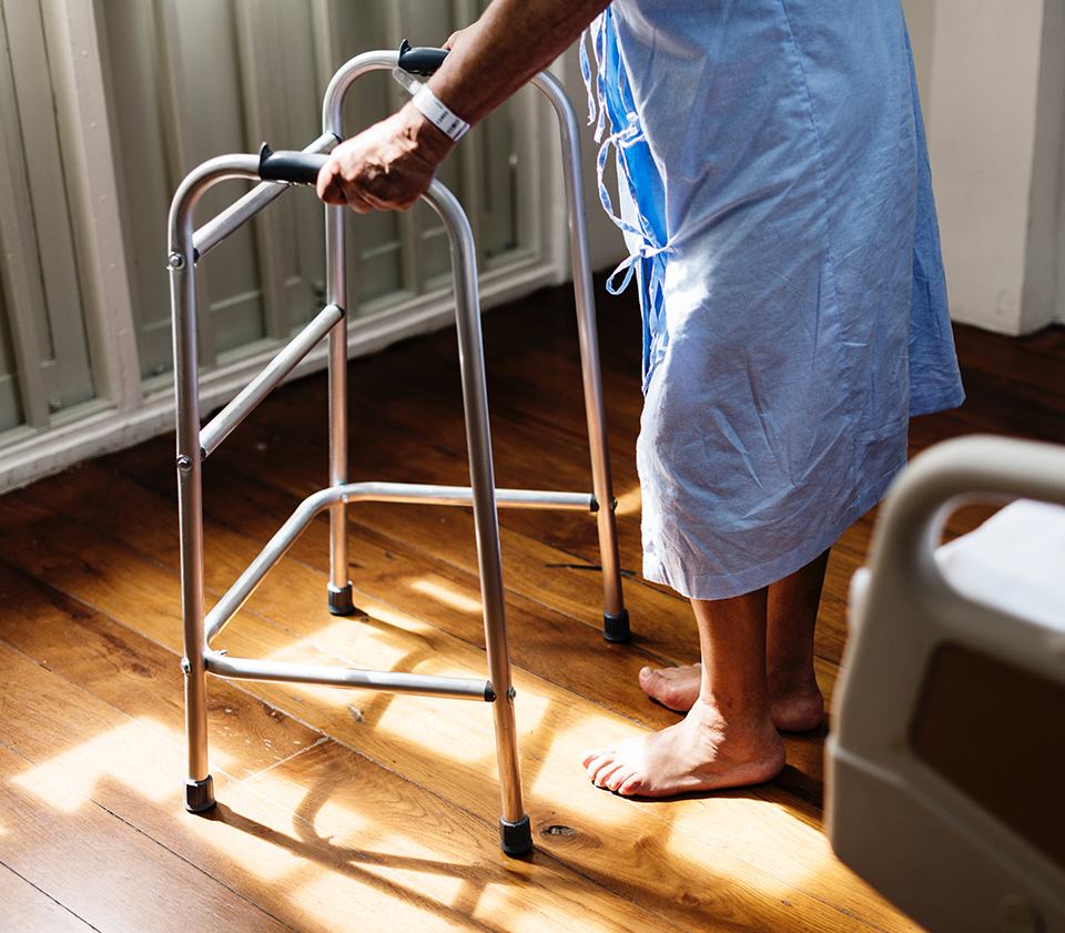 Man in hospital gown standing with the help of a walker