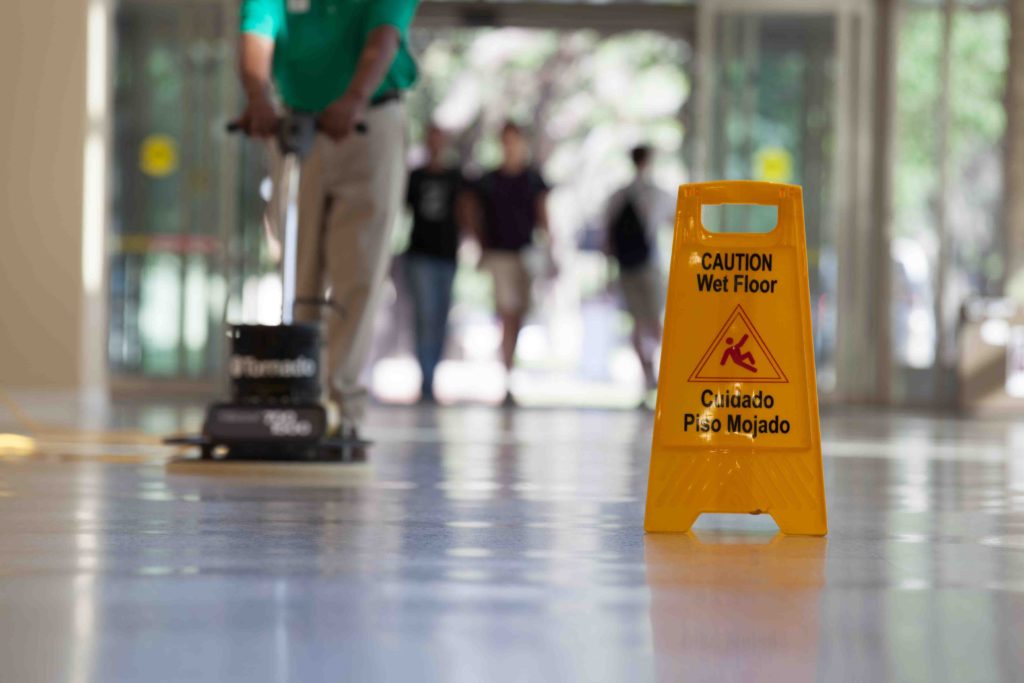 image of worker buffing floors with caution sign in fore-ground
